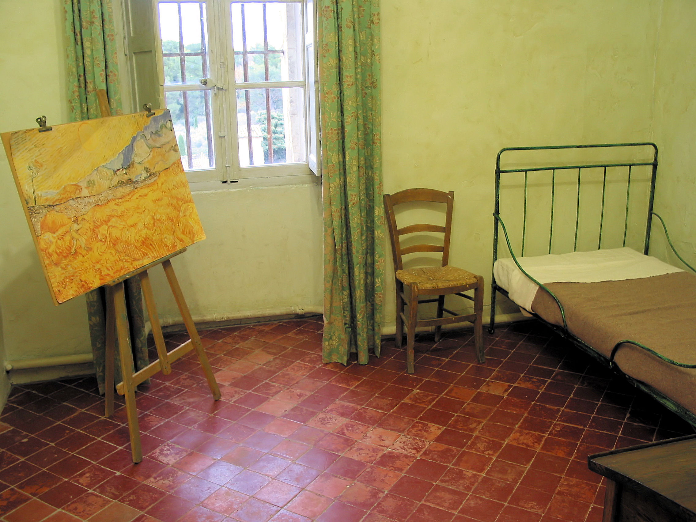 photograph of van gogh's bedchamber in the asylum, showing an easel on the left, a window in the center, and a bed on the right